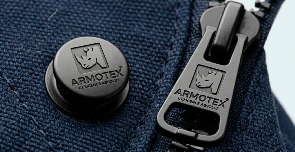Bouton et tirette de fermeture portant la signature ARMOTEX sur un tissu bleu marine